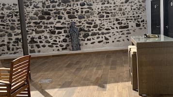 Un patio en la azotea con un muro de piedra, una estatua, muebles de mimbre y una silla de madera.