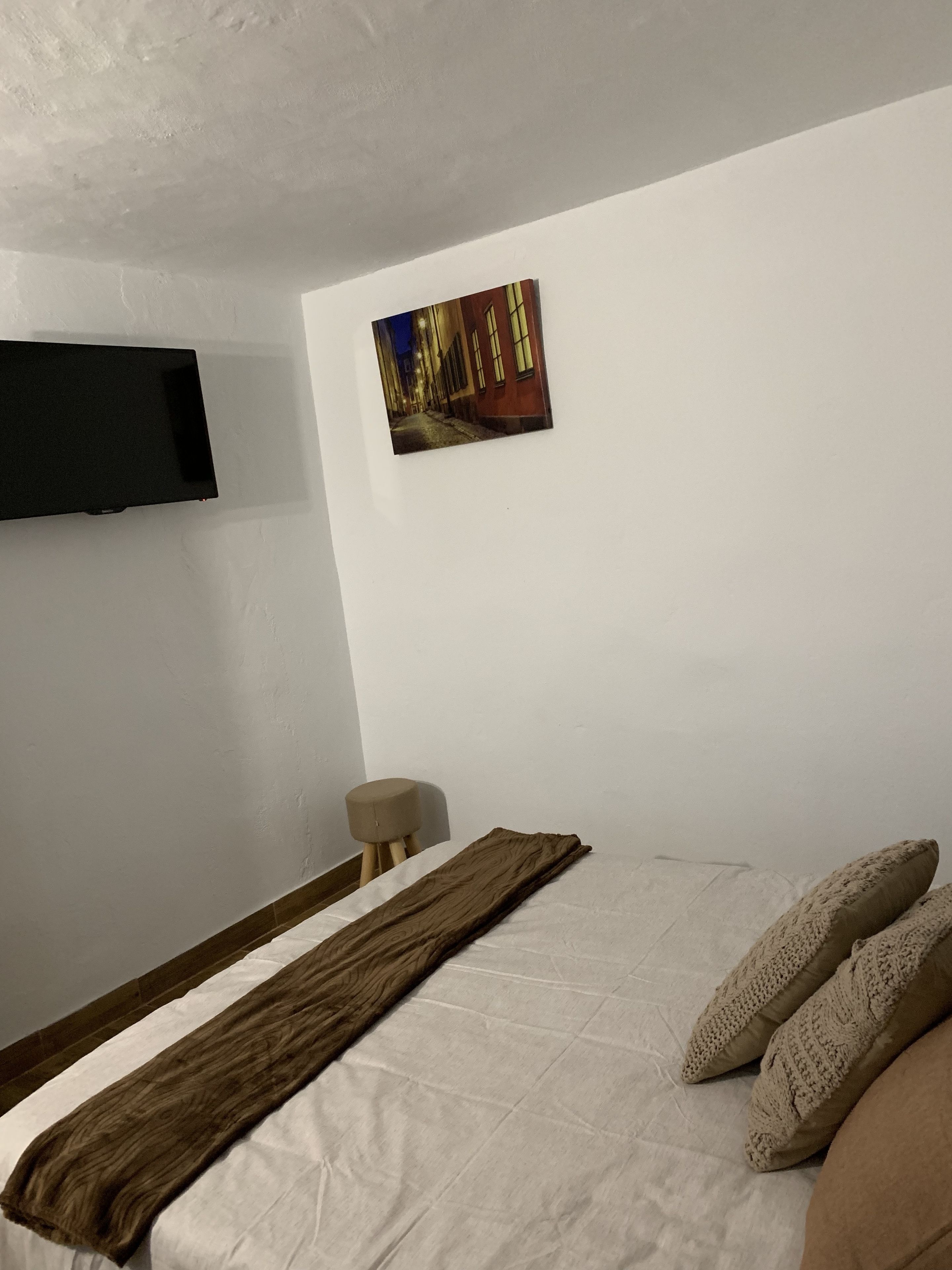 A bedroom with a bed, a mounted TV, a wooden floor, and a wall-mounted picture.