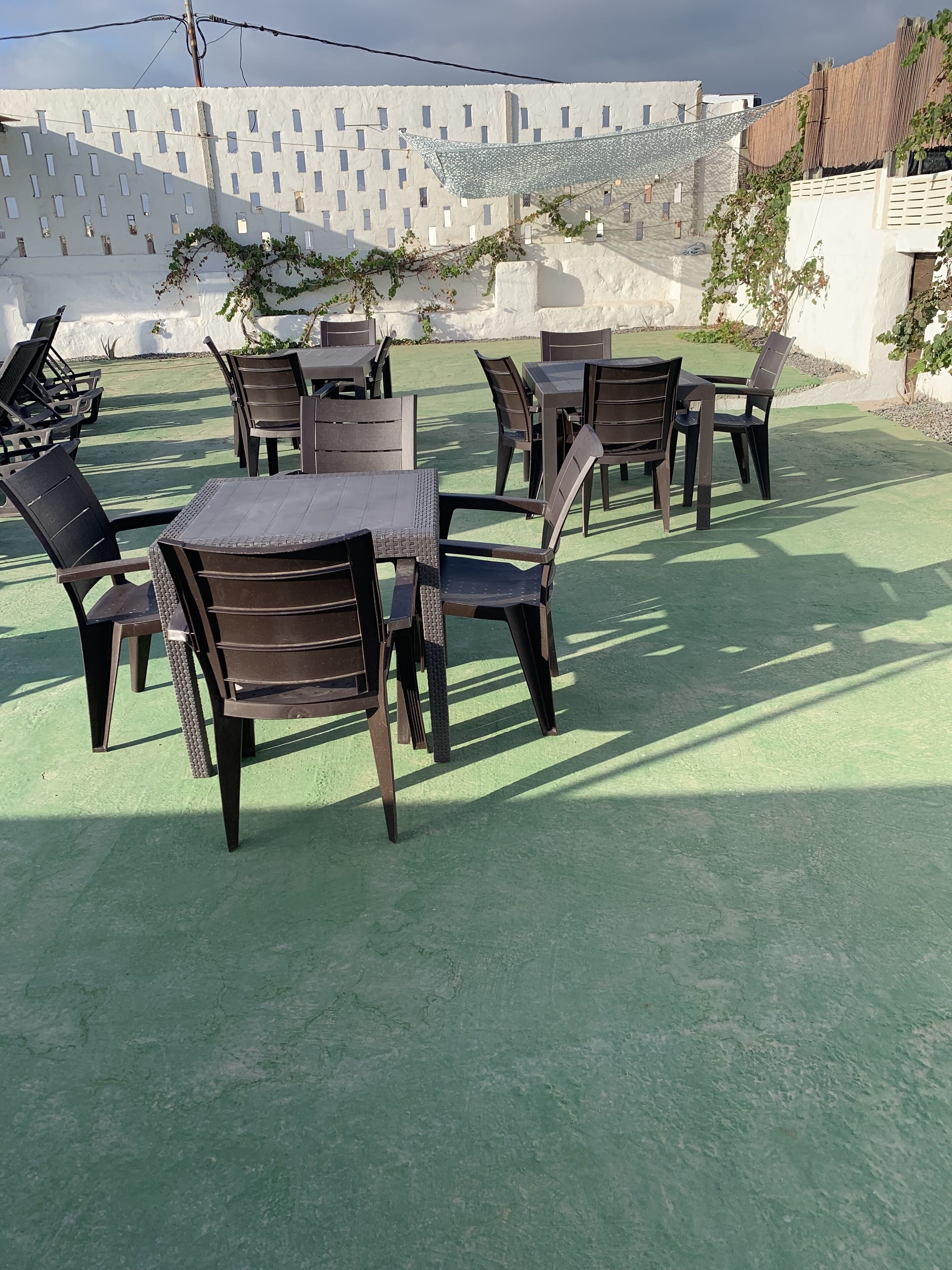 Outdoor seating with tables and chairs, a white wall with windows, and a green ground cover.