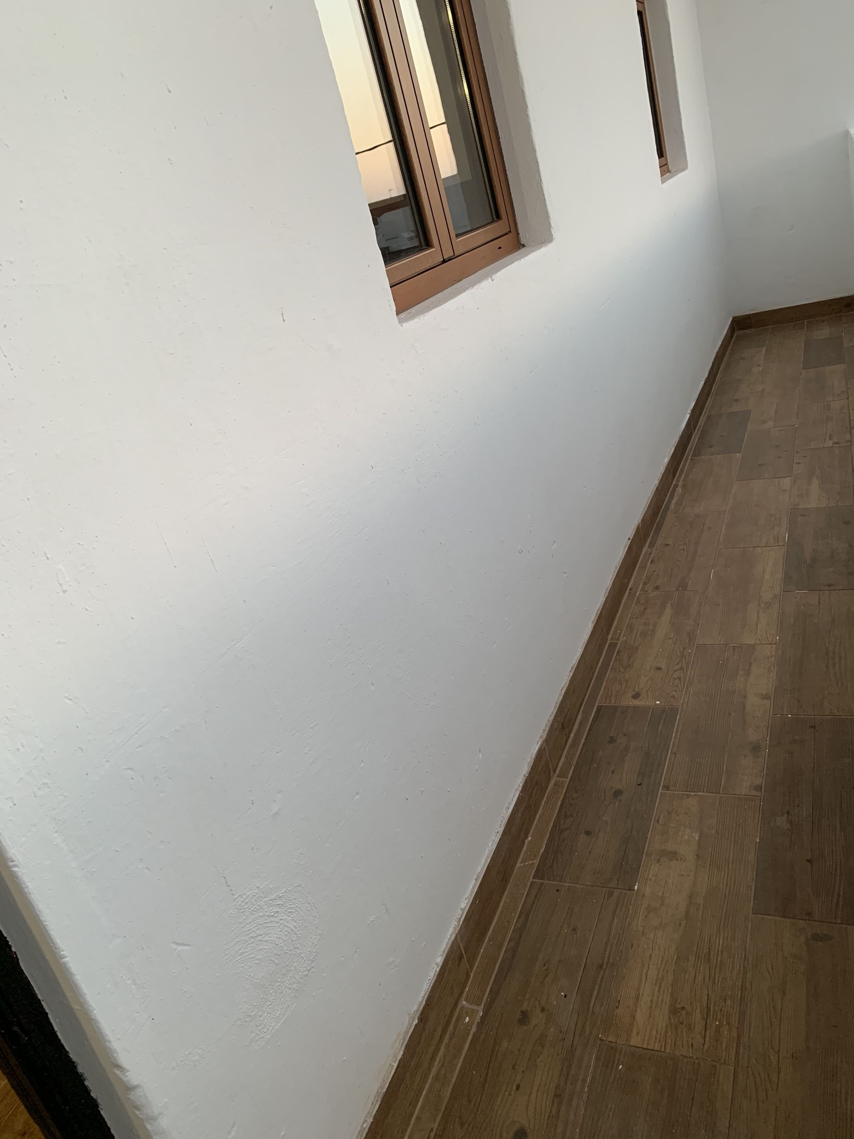 Een kamer met witte muren, een houten vloer en een raam met houten kader.