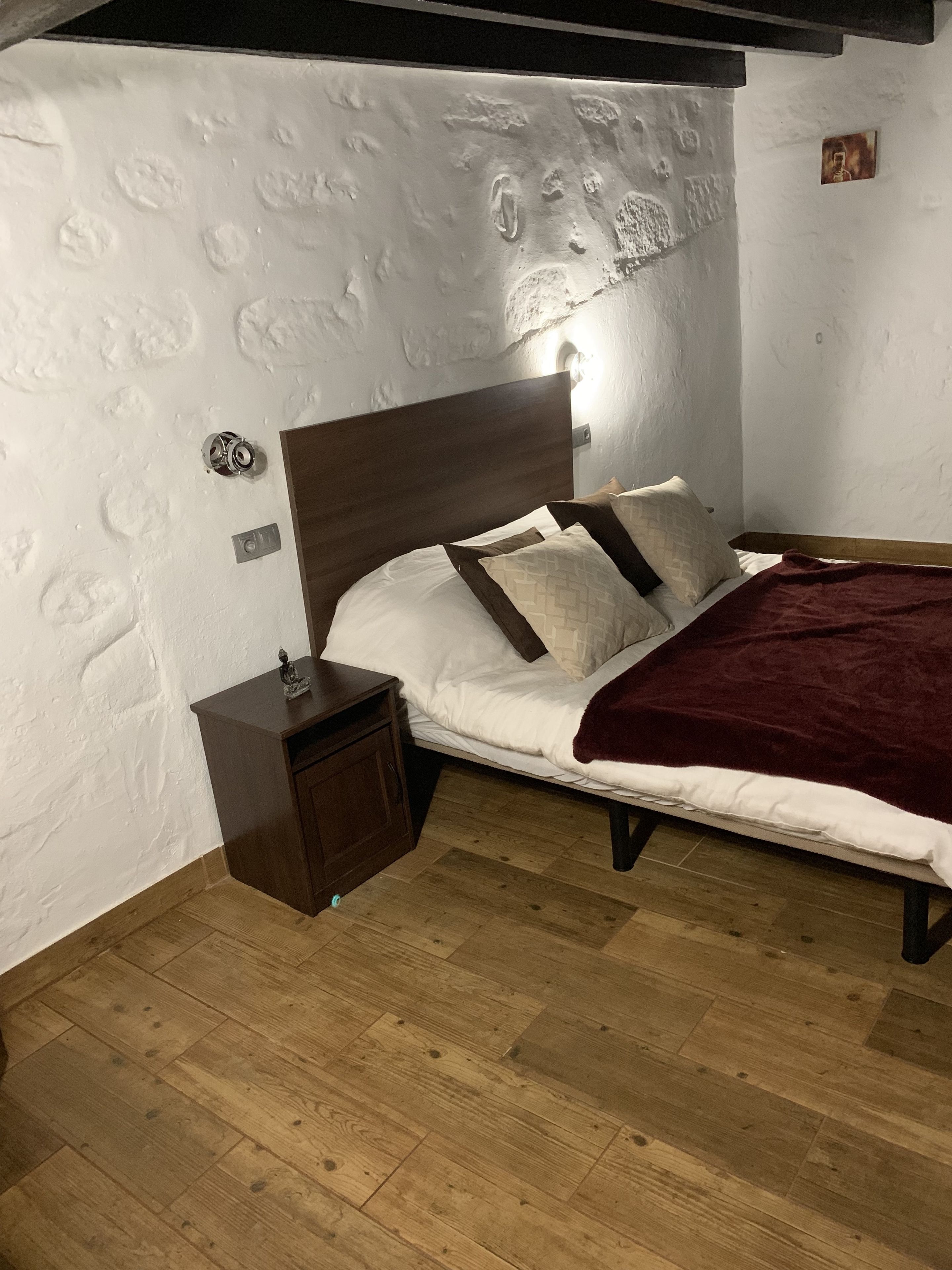 A bedroom with a wooden bed, white walls with a textured pattern, a nightstand, and a red blanket.