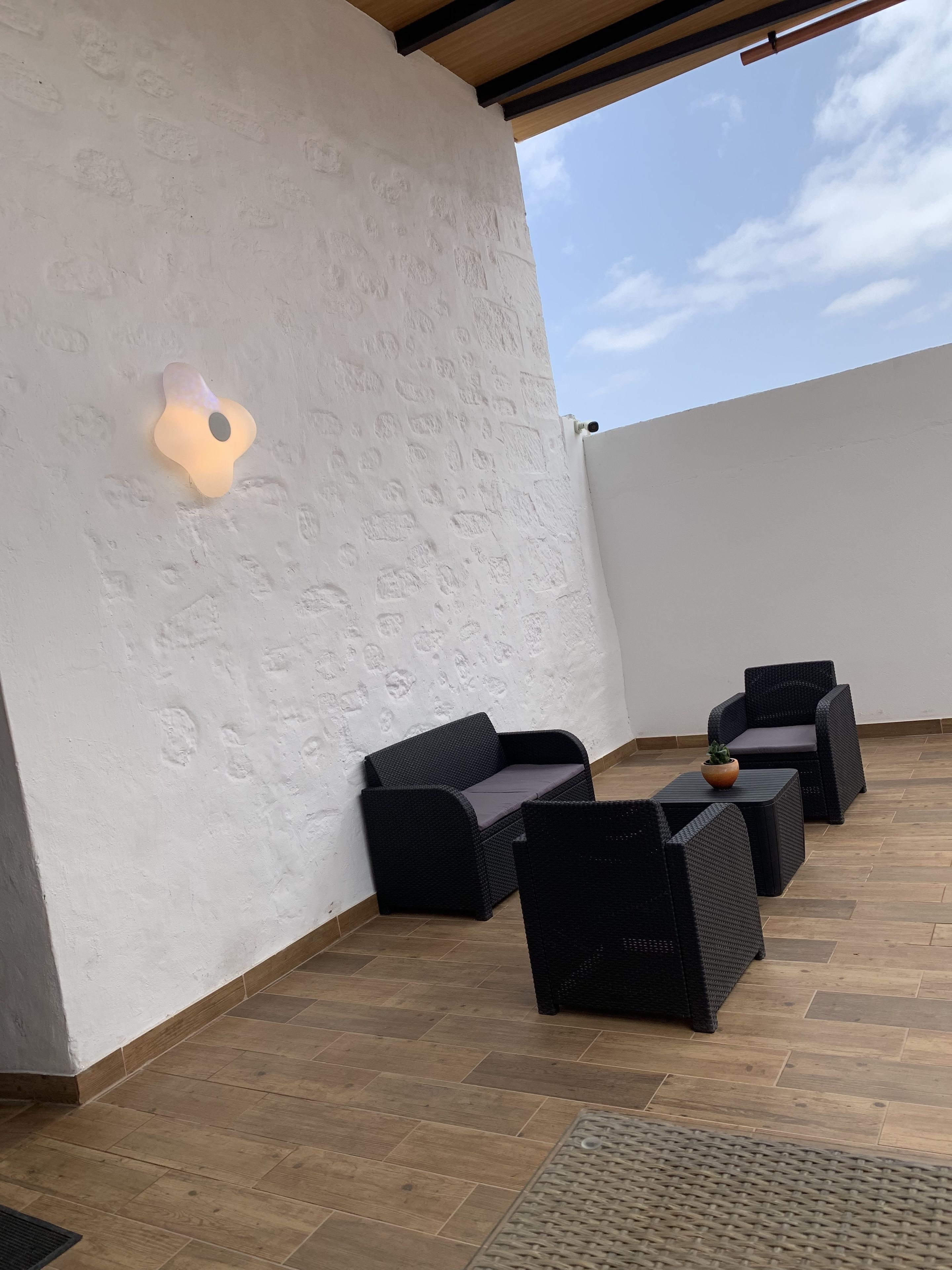 En tagterrasse med en hvid væg med struktur, en lampe og møbler i sort flet.