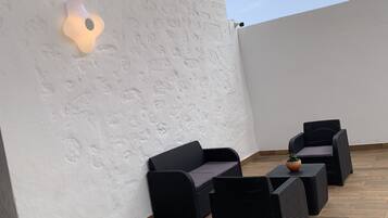 En tagterrasse med en hvid væg med struktur, en lampe og møbler i sort flet.