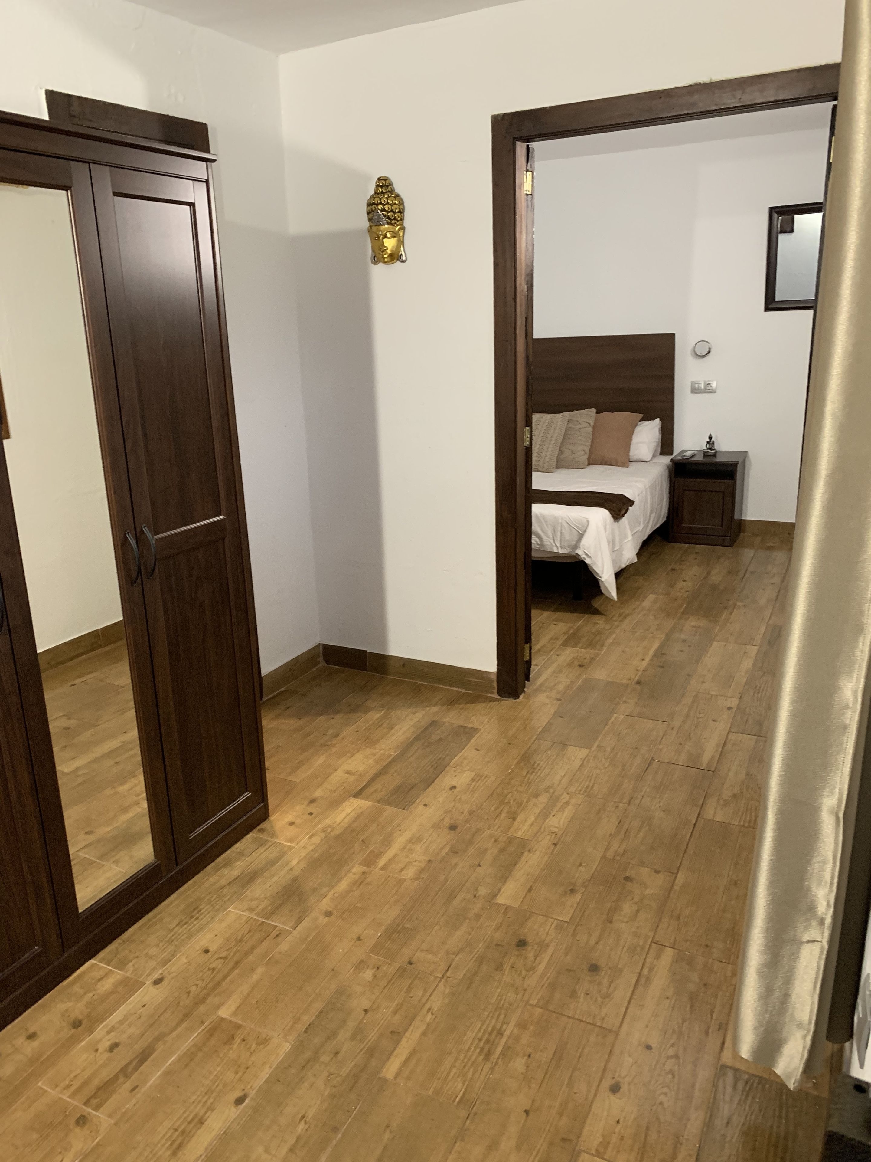 Une chambre avec un plancher en bois, un lit avec une literie blanche, une table de chevet et une statue de Bouddha fixée au mur.