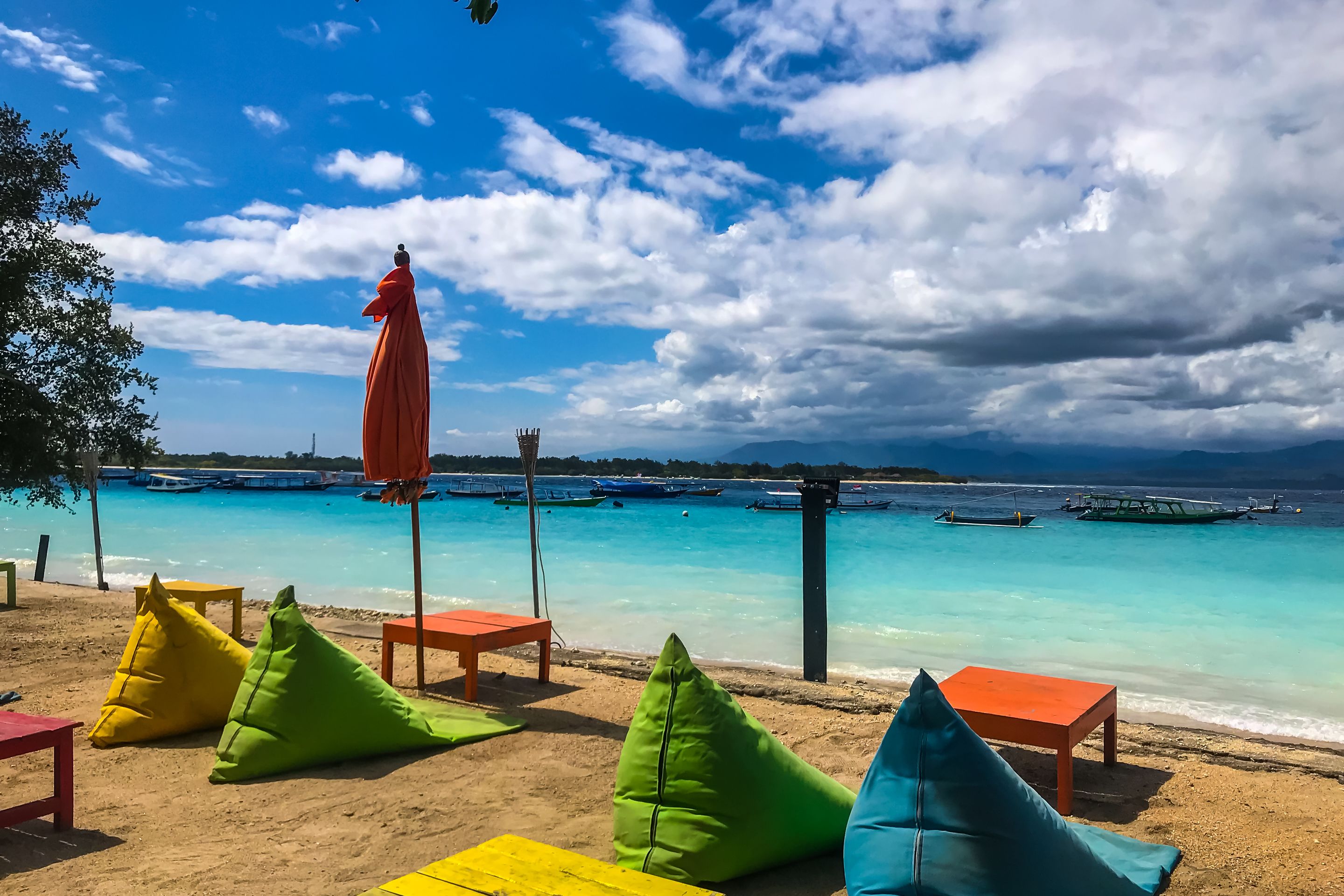 A beach with colorful seating, a statue, and boats in the background.