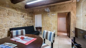 A stone-walled room with a wooden table, striped chairs, a black sofa, a TV, and a door leading to another room. - Vallettastay Banoffee (Valletta)