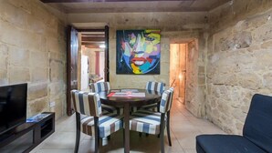 A dining area with a round table and striped chairs, a painting on the wall, and a TV on the left. - Vallettastay Banoffee (Valletta)