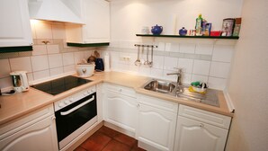 Una cocina compacta con armarios blancos, una estufa, un horno, un lavamanos y una encimera.