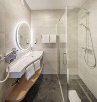 Un baño moderno con ducha de vidrio, tocador con espejo y repisa de madera.