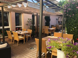 Un área de patio al aire libre con muebles de mimbre, plantas en macetas y una pérgola que proporciona sombra.