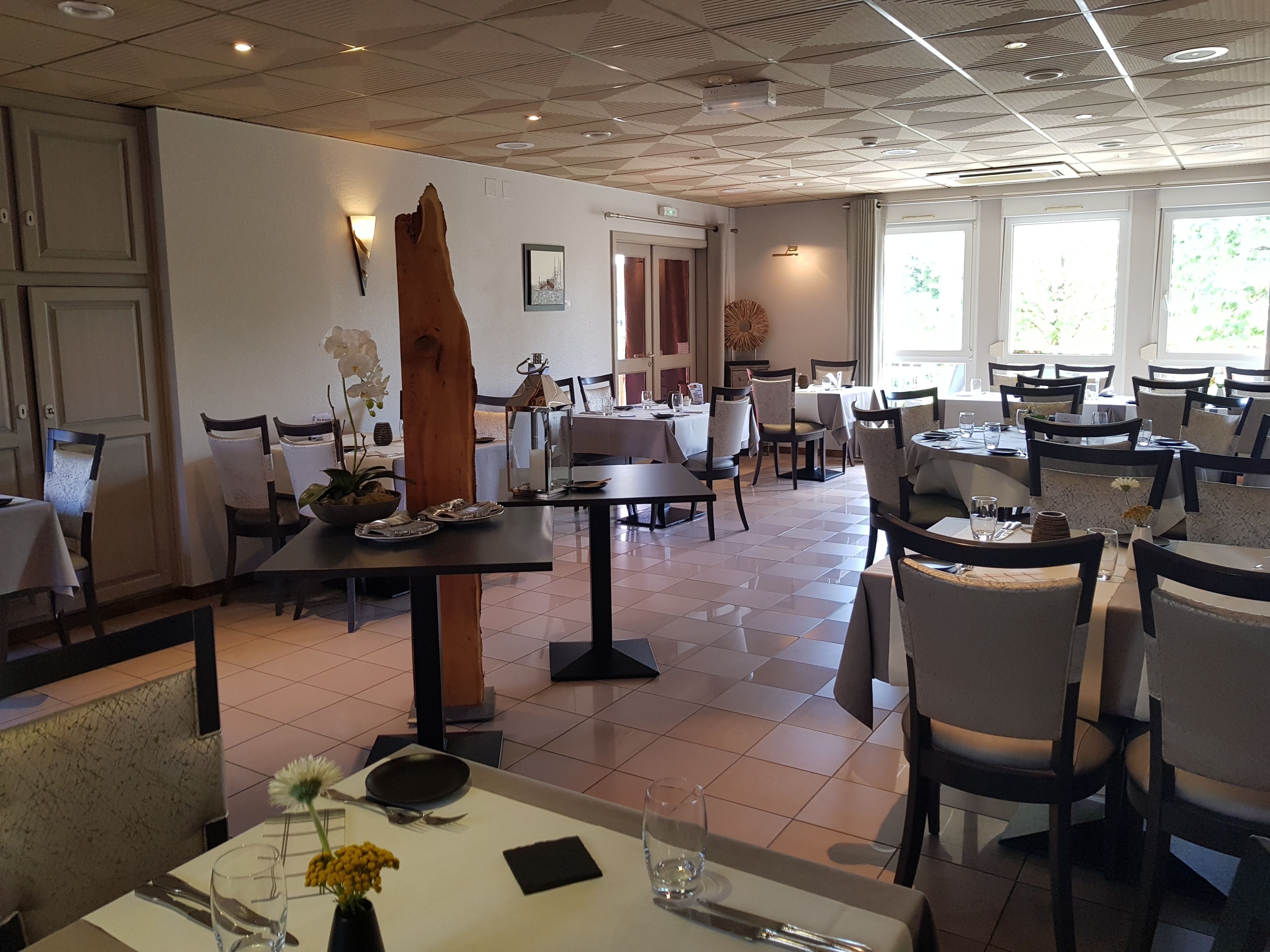 Un restaurante con varias mesas y sillas, una gran escultura de madera y vistas a zonas verdes a través de las ventanas.