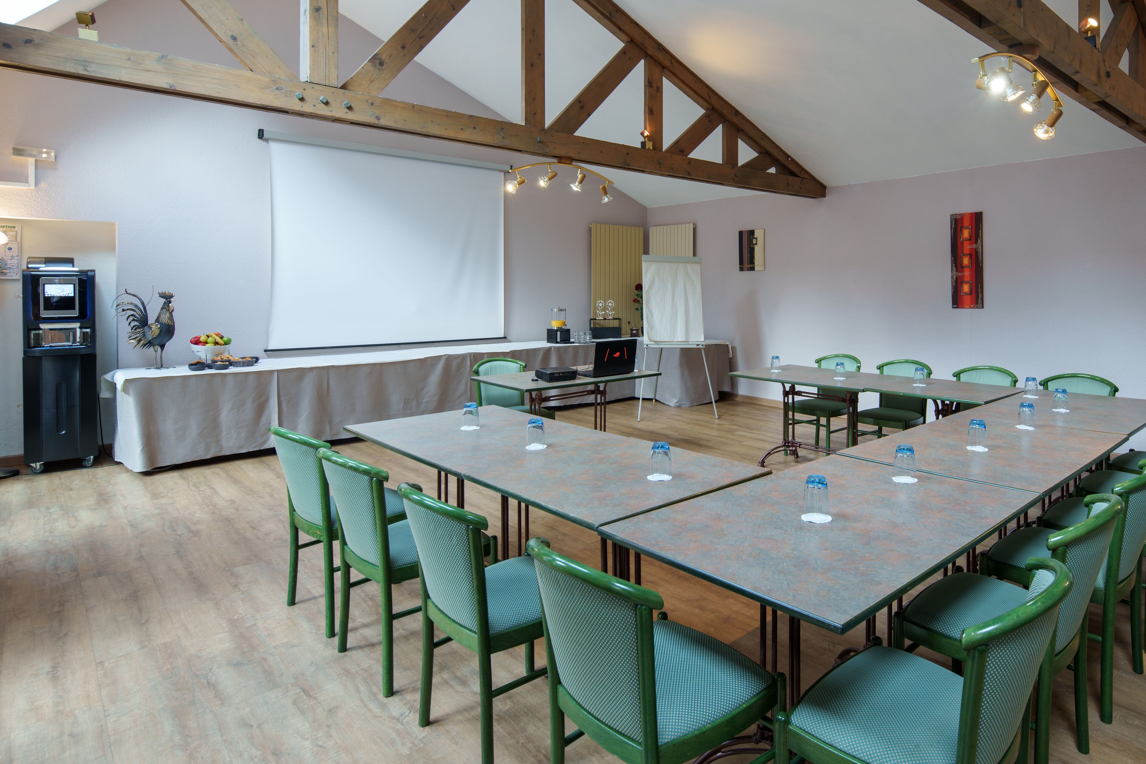 A conference room with a long table, green chairs, a projector screen, and a wooden ceiling.