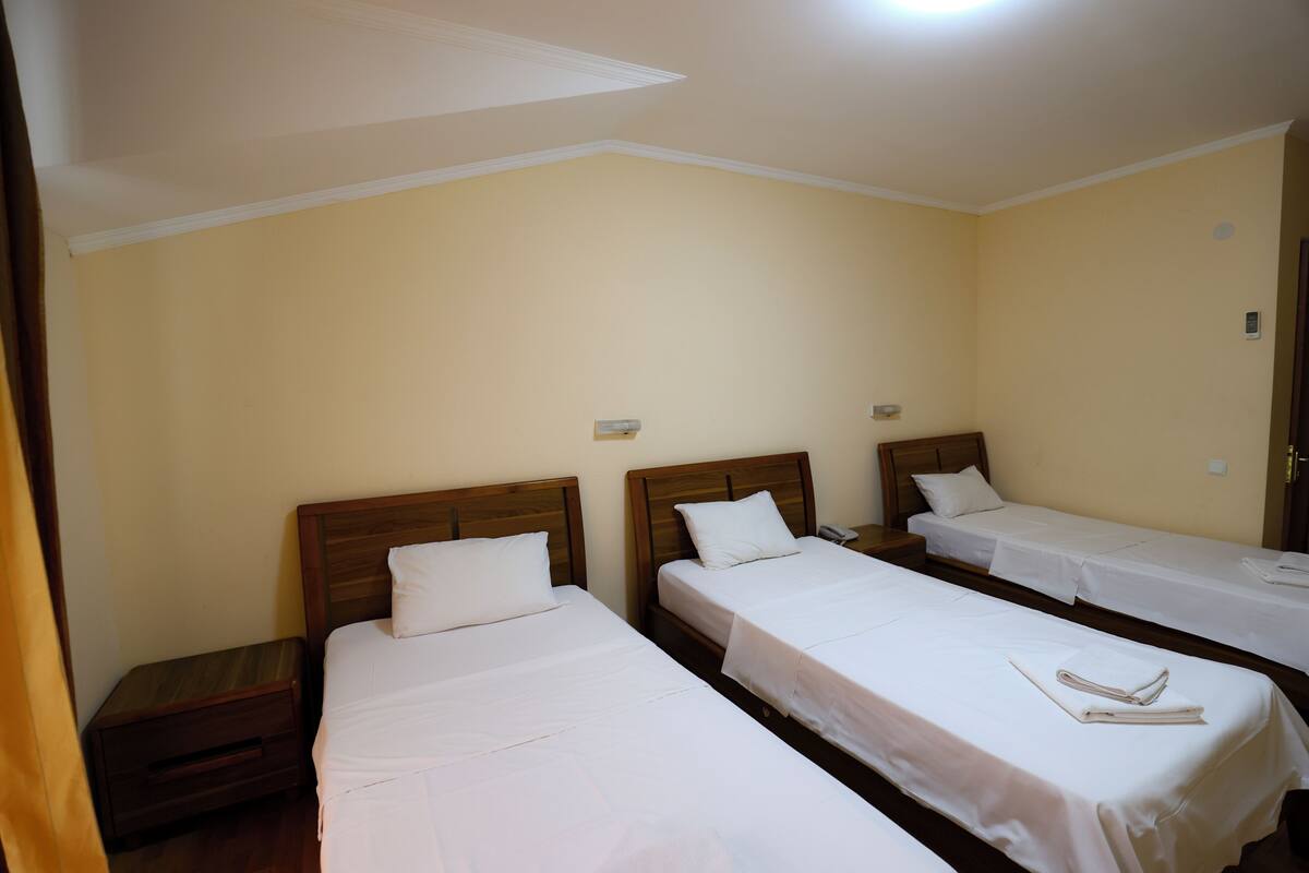 Une chambre d’hôtel avec trois lits simples, des têtes de lit en bois et du linge de lit blanc.