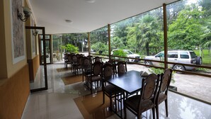 Amplio espacio interior con una larga mesa y sillas, grandes ventanales que ofrecen vistas a un estacionamiento y áreas verdes exteriores.