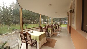 Un restaurante con mesas y sillas, ventanas amplias y vistas a un parque.