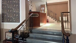Zona de recepción con un mostrador de madera, una escalera con barandilla metálica y una pared con estampado floral.