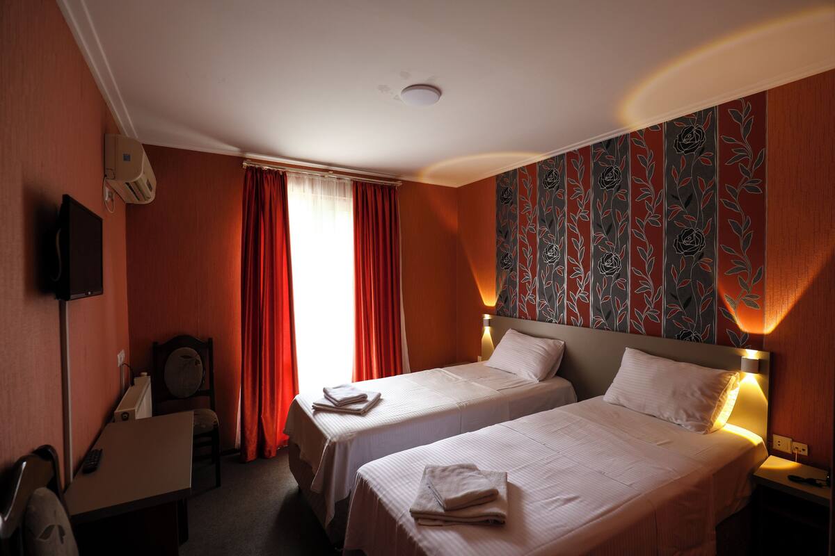 Une chambre d’hôtel avec deux lits, un bureau, une chaise, une télévision et une fenêtre avec des rideaux rouges.