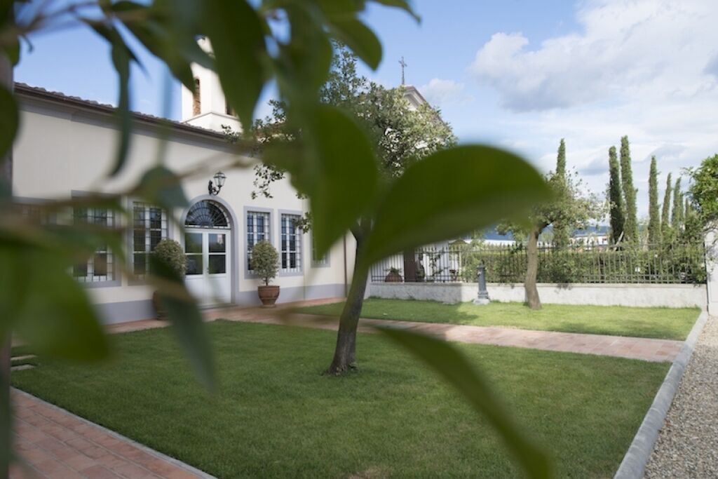 Une cour avec un bâtiment blanc, un petit arbre et une pelouse soigneusement entretenue.