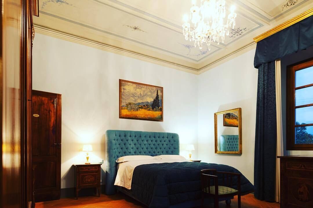 Ein Schlafzimmer mit einem großen Bett, einer Chandelier, einem Gemälde an der Wand und einem Fenster mit Vorhängen.