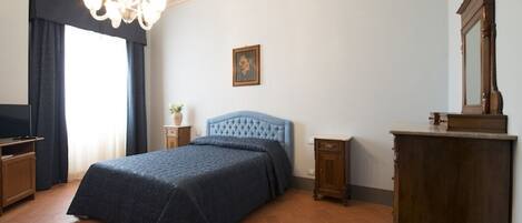 A bedroom with a large bed, a chandelier, a wooden dresser, and a television.