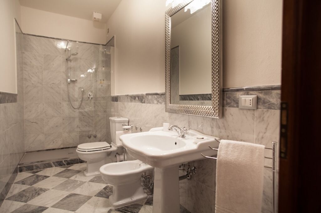A bathroom with a shower, toilet, bidet, sink, and a large mirror.