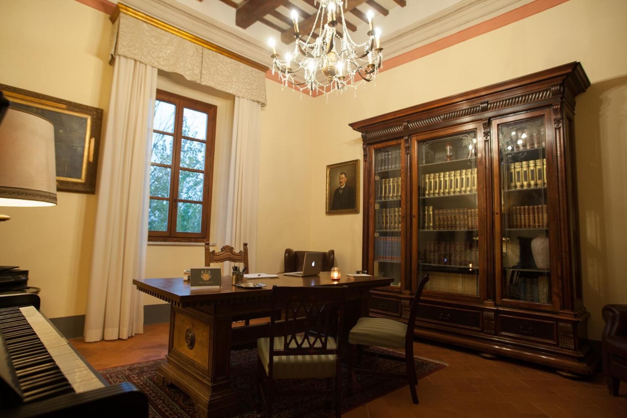 Ein eleganter Raum mit Klavier, Schreibtisch aus Holz, einer Chandelierleuchtre und einem Bücherregal.