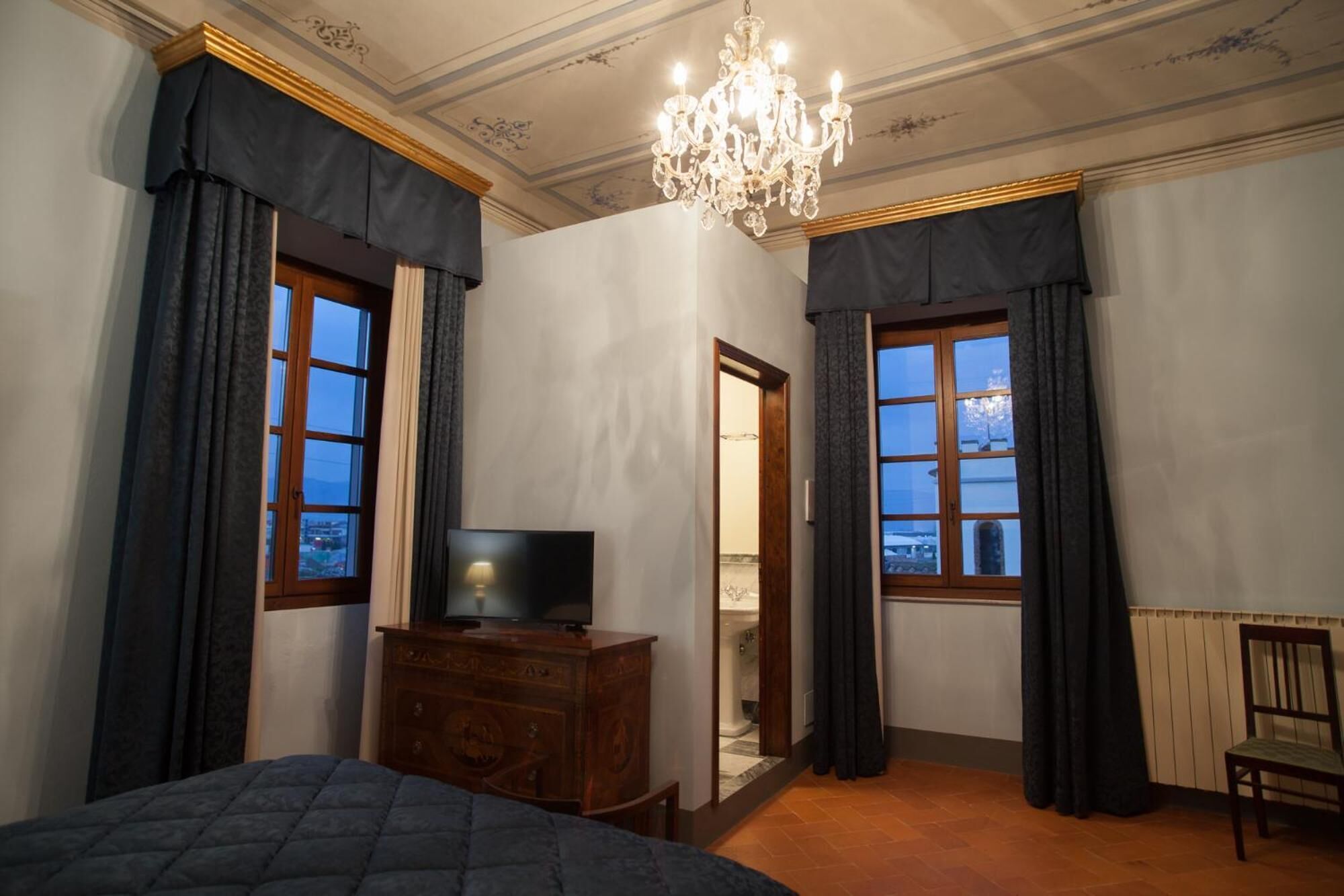 Un dormitorio con cama, cómoda, televisor y ventana con cortinas.