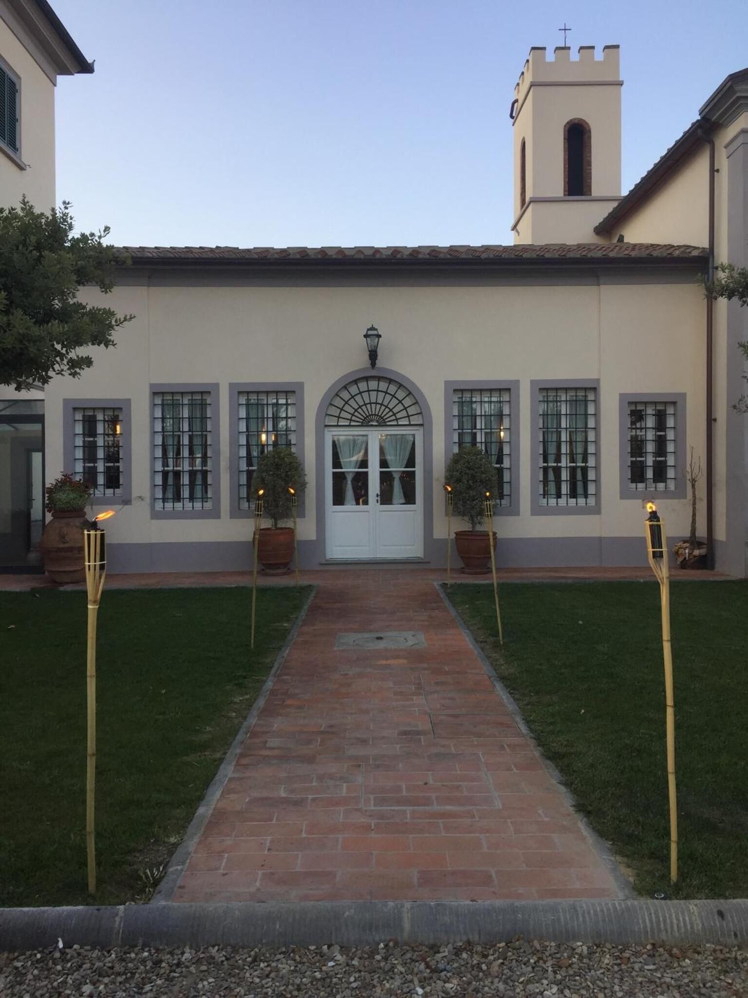 Un bâtiment doté d’une entrée centrale, flanqué de plantes en pot et éclairé par des torches.
