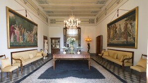 A grand room with a chandelier, two sofas, a table with flowers, and large classical paintings on the walls. - Relais Villa Scarfantoni B&B (Montemurlo)