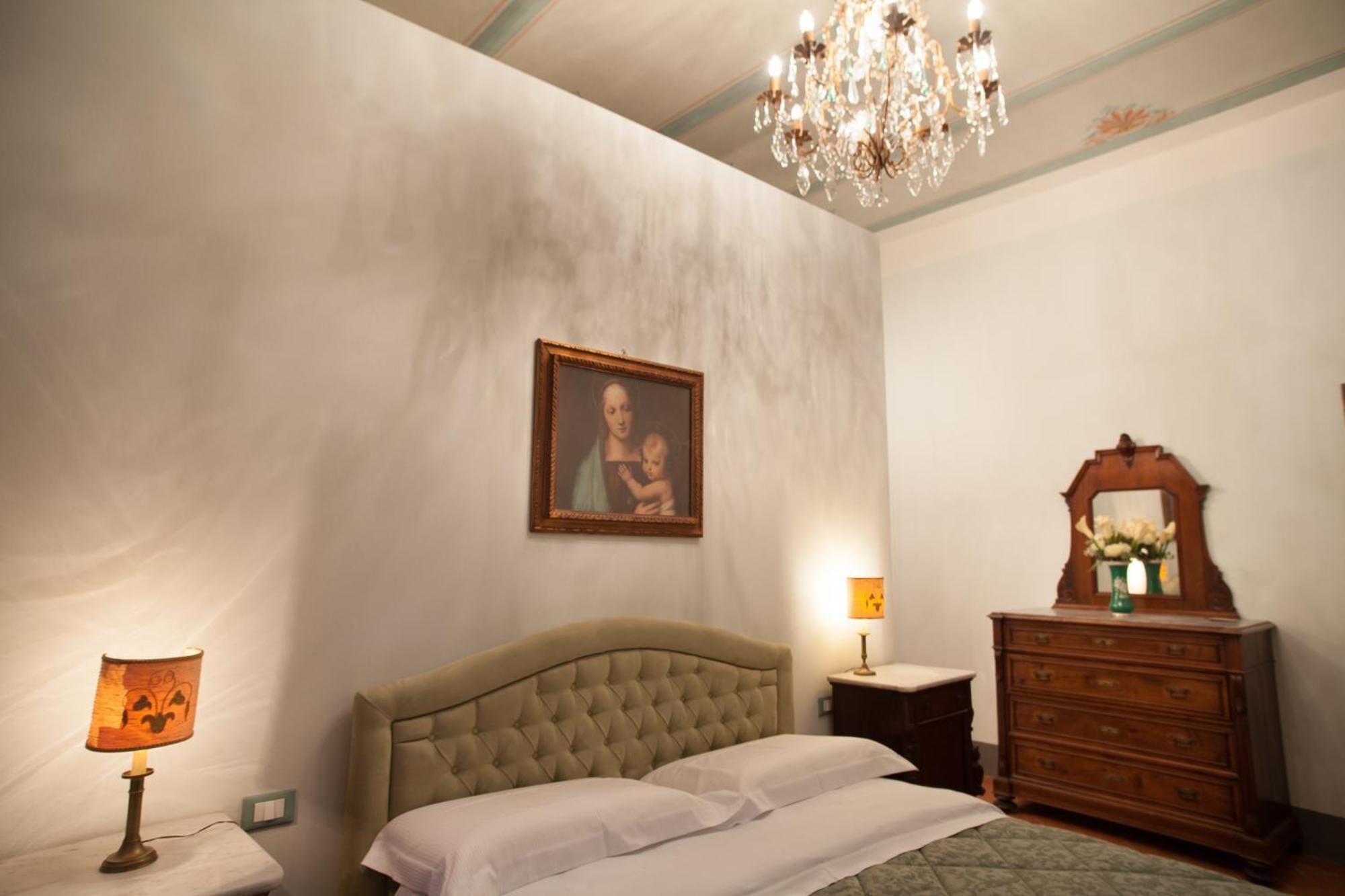 A bedroom with a large bed, a chandelier, a dresser, and a framed picture on the wall.