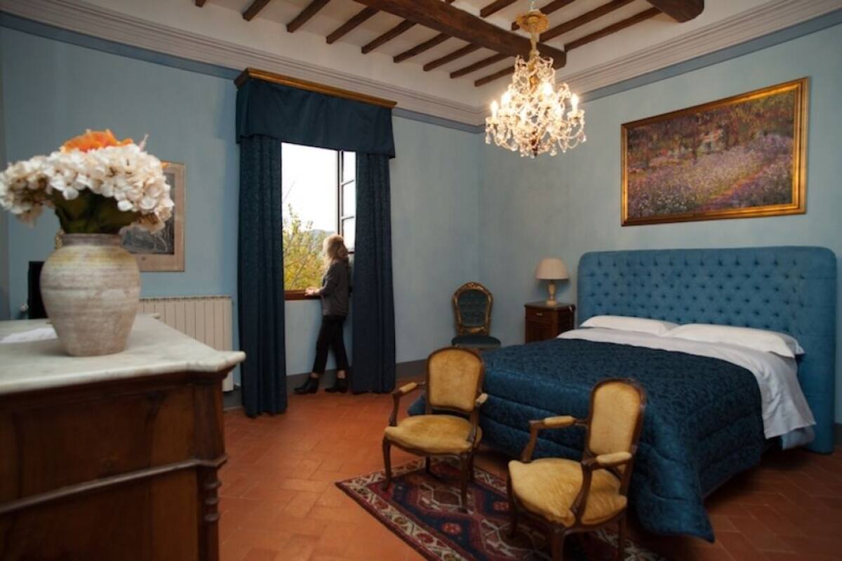 Een slaapkamer met een groot bed, een kroonluchter, een schilderij en een raam met gordijnen.