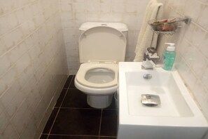A bathroom with a toilet, sink, and a glass soap dispenser. - Résidence Clara T4 (Abidjan)