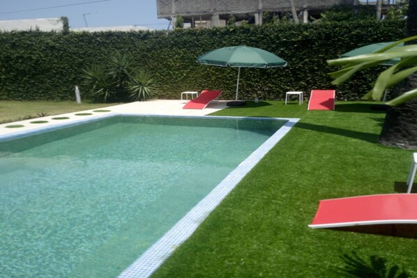 Una piscina al aire libre, sombrillas, sillones reclinables de piscina