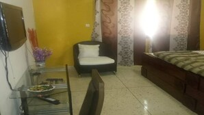 Un dormitorio pequeño con una cama, una silla, una mesita con un frutero y un televisor en la pared.