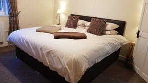 Un lit bien fait, avec du linge de lit blanc et marron, une tête de lit et une lampe de chevet.