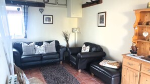 Un salon avec un canapé en cuir noir, un meuble en bois et un sol carrelé.
