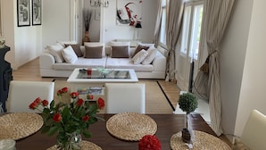 Uma sala de estar moderna com um sofá branco, uma mesa de centro de vidro e uma mesa de jantar com jogos americanos trançados.