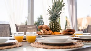 Une table de petit-déjeuner avec des assiettes remplies de nourriture, notamment un ananas, des croissants et du jus d’orange.