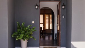 Une entrée moderne agrémentée d’une plante en pot, d’une porte sombre et d’un sol carrelé qui mène à un espace intérieur.