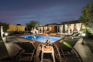Un área junto a la piscina con sillones de descanso, una piscina y un edificio de fachada de vidrio.