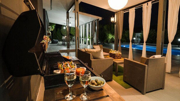 Une terrasse extérieure avec un barbecue, des meubles en osier et une piscine en arrière-plan.