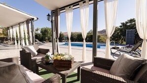 Un espace extérieur aménagé, abrité et doté de mobilier en osier, une piscine et une vue sur le paysage.