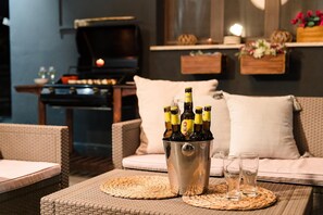 A cozy living area with wicker furniture, a grill, and a bucket of beer bottles.