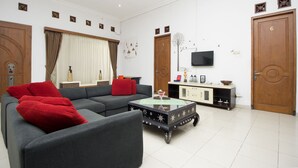 Un salon avec un canapé gris, des coussins rouges, une table basse, un téléviseur et des portes en bois.