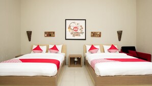 Une chambre d’hôtel avec deux lits, chacun agrémenté de draps rouges et blancs, une œuvre d’art encadrée au mur et une petite table placée entre les lits.
