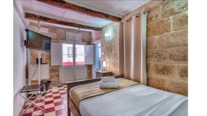 Una habitación con cama, una mesita, televisor y ventana con cortinas.