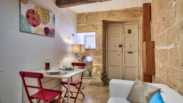 Una habitación acogedora con un sofá blanco, una mesa de comedor con sillas rojas, un cuadro en la pared y una pared de piedra.