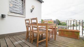 Una terraza de madera con una mesa, sillas, una maceta y un ventanal con un celosía decorativa.