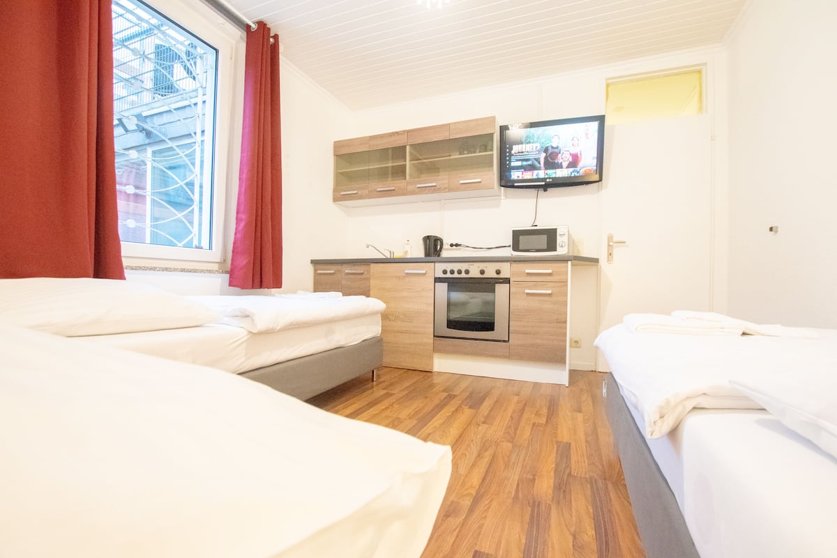A hotel room with two beds, a kitchenette with a microwave, oven, and a TV mounted on the wall.