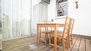 A wooden table and chairs on a wooden deck with a white wall and a window with a metal grid. - Lovely City House (Meerbusch)